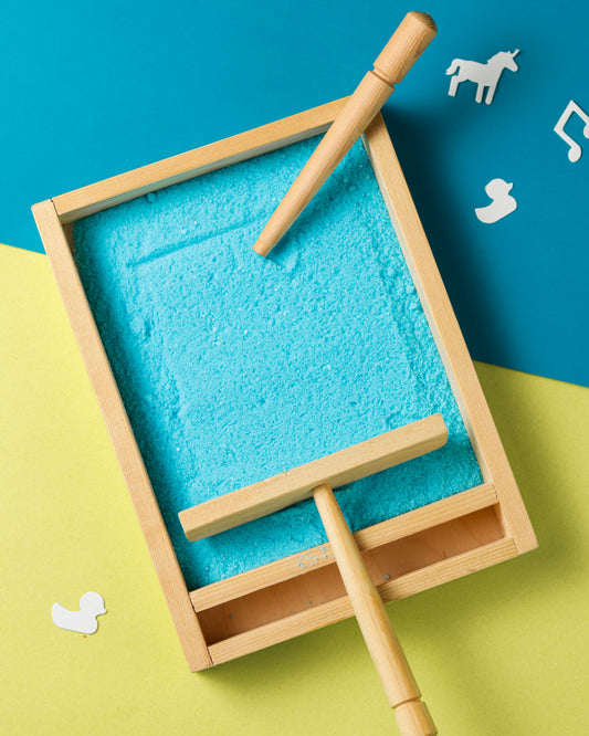 Wooden sand tray with blue salt and wooden tools on a colorful background
