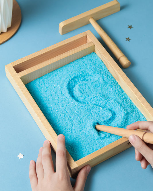 Wooden tray with blue salt (sand), being shaped by hands on a blue background