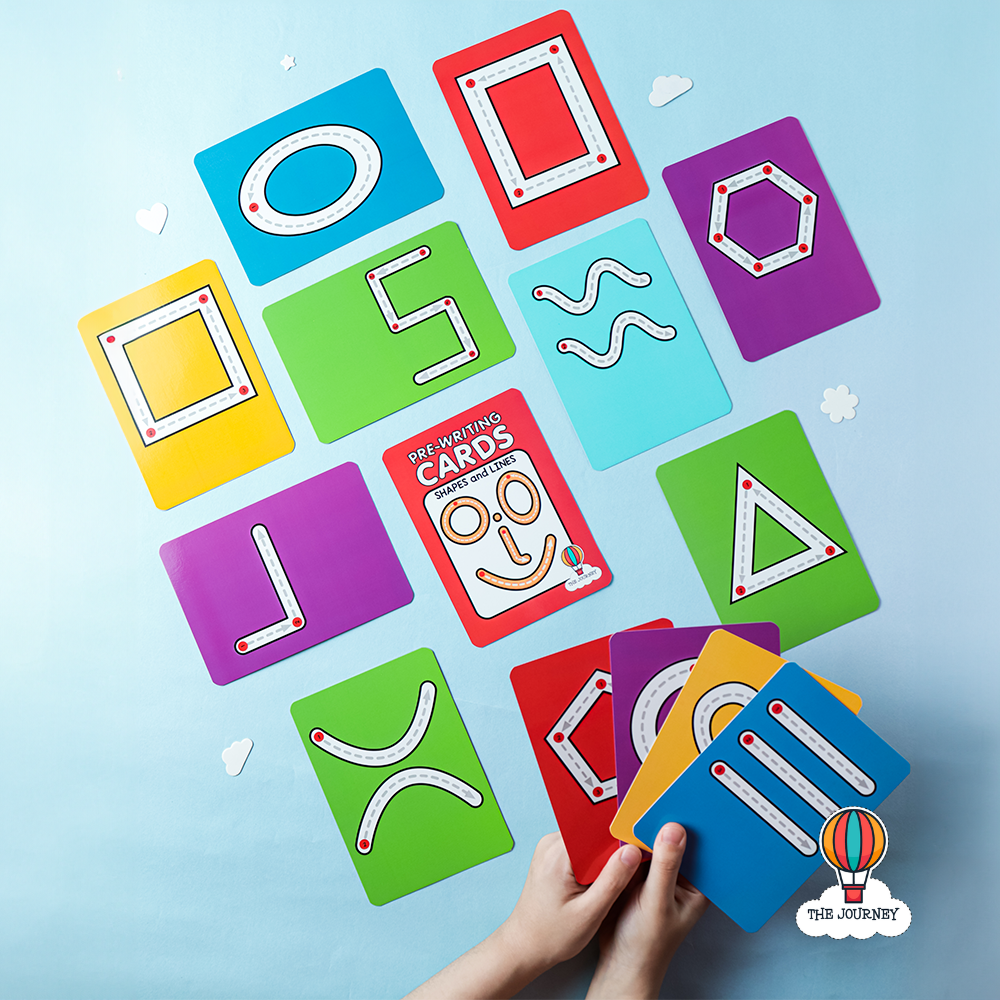 A set of colorful educational flashcards with various shapes and lines for pre-writing practice, held in a child's hand.