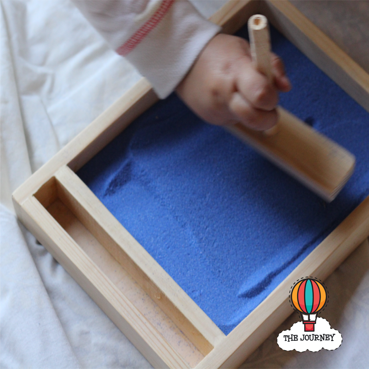 Sand tray with geometric lines and shapes and a hand using a tool, with 'The Journey' branding.